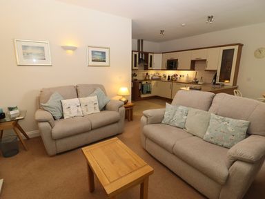 A living room with two sofas, cushions, a wooden coffee table, and a kitchen area in the background at Tethera in Keswick