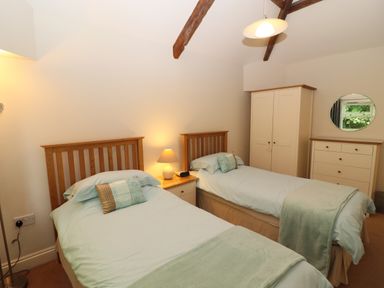 A bedroom with two single beds a nightstand with a lamp a wardrobe a chest of drawers and a round mirror at Tethera in Keswick