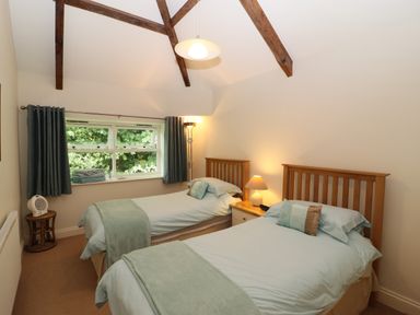 A bedroom with two single beds with wooden headboards a bedside table with a lamp a window with curtains and exposed ceiling beams at Tethera in Keswick