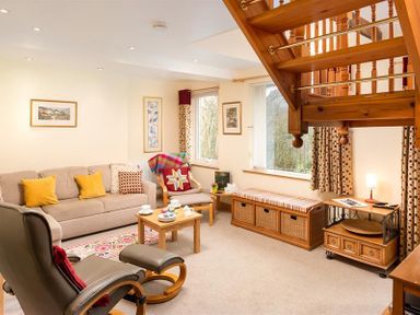 A living room with a beige sofa and yellow cushions a wooden coffee table and armchair under wooden stairs at Lingmoor View in Chapel Stile