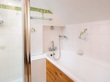 A bathroom with a white bathtub wood paneling shower area and white tiled walls with green border at Lingmoor View in Chapel Stile