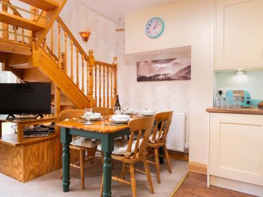A dining area with a wooden table set for four near a wooden staircase and a kitchen counter at Lingmoor View in Chapel Stile