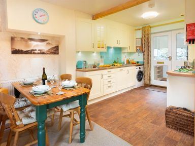 A kitchen with a wooden dining table and chairs a washing machine and cupboards at Lingmoor View in Chapel Stile
