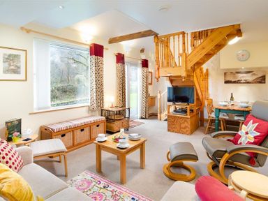 A living room with wooden stairs a television a dining table and chairs and patterned curtains at Lingmoor View in Chapel Stile