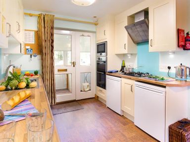 A kitchen with wooden countertops white cabinets a stove a microwave and a door with a cat flap at Lingmoor View in Chapel Stile