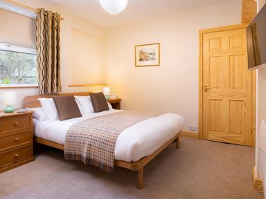 A bedroom with a double bed two brown pillows bedside tables with lamps wooden door and window with curtains at Lingmoor View in Chapel Stile
