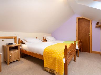 A bedroom with two wooden single beds with white bedding a yellow and green throw a wooden nightstand and a wooden door at Lingmoor View in Chapel Stile
