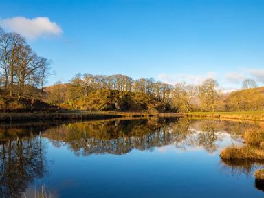 A lake with reflections of trees and hills under a blue sky at Lingmoor View in Chapel Stile