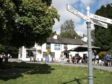 A street view of a white building with outdoor seating and people near a road sign with directions at Lingmoor View in Chapel Stile
