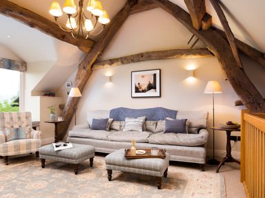 A living room with a sofa chair two ottomans and wooden beams at High Cunsey Farm in Far Sawrey
