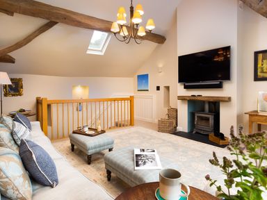 A living room with a sofa, ottomans, a wood stove, and a mounted TV at High Cunsey Farm in Far Sawrey