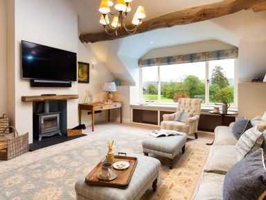 A living room with a sofa armchair ottomans a fireplace and a large window at High Cunsey Farm in Far Sawrey