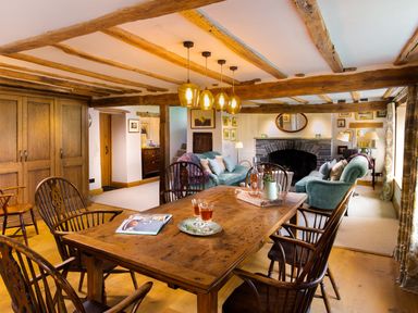 A dining area with a wooden table and chairs next to a living area with sofas and a fireplace at High Cunsey Farm in Far Sawrey