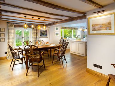A dining area with a wooden table and chairs next to a kitchen with white cabinets at High Cunsey Farm in Far Sawrey