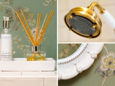 A shower head and toiletries on a tray with floral wallpaper and a decorative mirror frame at High Cunsey Farm in Far Sawrey