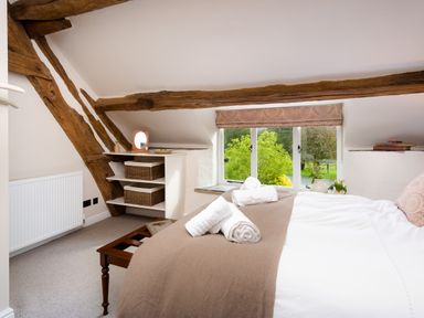 A bedroom with a bed, wooden beams, a window with a view of greenery, and shelves with baskets at High Cunsey Farm in Far Sawrey