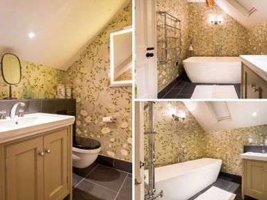 A bathroom with a bathtub, sink with cabinet, wall mirror, toilet, and floral wallpaper at High Cunsey Farm in Far Sawrey