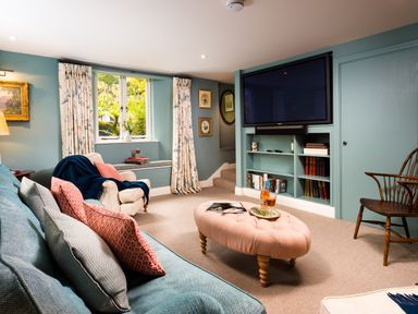 A living room with a blue sofa decorated with pillows a pink ottoman and a TV on the wall at High Cunsey Farm in Far Sawrey