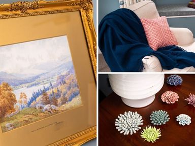 A framed landscape painting a beige armchair with a blue throw and a patterned pillow and decorative ceramic flowers on a wooden surface at High Cunsey Farm in Far Sawrey