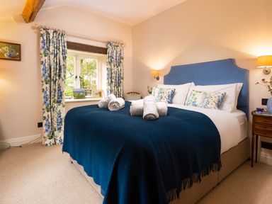 A bedroom with a double bed with blue headboard and blanket and floral curtains at High Cunsey Farm in Far Sawrey