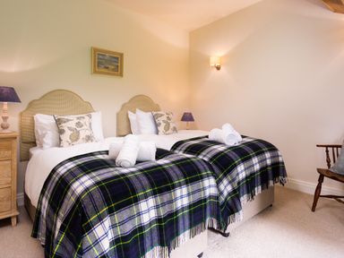 A bedroom with two single beds covered with plaid blankets and rolled towels at High Cunsey Farm in Far Sawrey