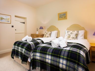 A bedroom with two single beds with plaid blankets and rolled towels at High Cunsey Farm in Far Sawrey