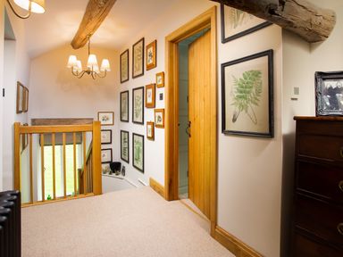 A hallway with framed botanical prints on the wall a wooden door a wooden railing and a chandelier at High Cunsey Farm in Far Sawrey