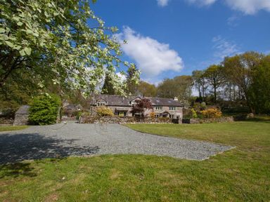 A stone house with a gravel driveway and grassy lawn surrounded by trees at High Cunsey Farm in Far Sawrey