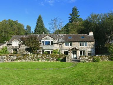 A stone house with multiple windows and a green lawn in front surrounded by trees at High Cunsey Farm in Far Sawrey