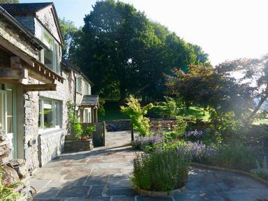Stone house with large windows and a paved patio with plants and trees at High Cunsey Farm in Far Sawrey