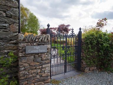 An iron gate attached to stone walls with a sign reading High Cunsey Farm and plants around the entrance at High Cunsey Farm in Far Sawrey