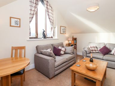 A living room with two sofas cushions a wooden coffee table and a round wooden dining table with chairs at Squirrel Bank in Ambleside