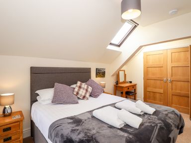 A bedroom with a bed, bedside tables, a dressing table, skylight, and double wooden doors at Squirrel Bank in Ambleside