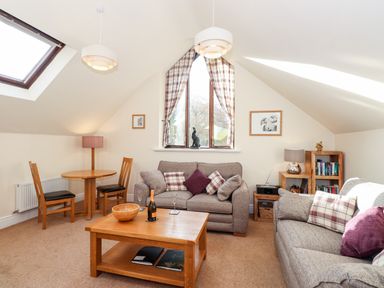 A living room with two sofas, a wooden coffee table, dining table with two chairs, bookshelf, and a window with curtains at Squirrel Bank in Ambleside