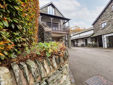A stone building with a balcony and a driveway next to other stone and white buildings at Squirrel Bank in Ambleside