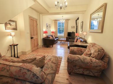 A living room with floral armchairs leather sofas wooden floor and a wood stove at Fairy Glen in Grasmere near Ambleside