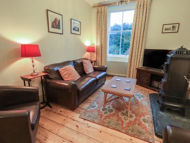 A sitting room with leather chairs a wooden coffee table a television and a wood stove at Fairy Glen in Grasmere near Ambleside