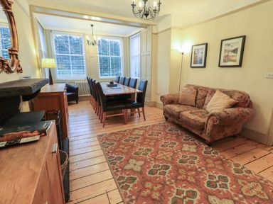 A dining room with a long wooden table and chairs a floral sofa and a patterned rug at Fairy Glen in Grasmere near Ambleside