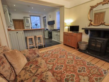 A living room with a floral sofa a patterned rug a fireplace and an open kitchen with stools at Fairy Glen in Grasmere near Ambleside
