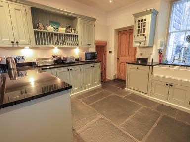A kitchen with stone tile floor cupboards and countertop with toaster microwave kettle and sink at Fairy Glen in Grasmere near Ambleside
