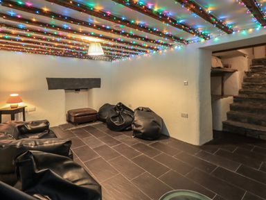 A basement room with black bean bag chairs a small table with a lamp a brown ottoman stone steps and colored string lights on the ceiling at Fairy Glen in Grasmere near Ambleside