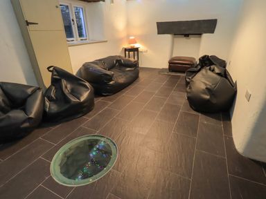 A room with black bean bag chairs a small table lamp a brown ottoman and a round glass floor window at Fairy Glen in Grasmere near Ambleside