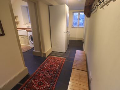 A hallway with a wooden bench a red patterned rug a refrigerator a washing machine and a kitchen sink at Fairy Glen in Grasmere near Ambleside
