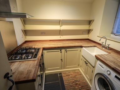 A kitchen with wooden countertops a gas stove a sink washing machine and wall shelves at Fairy Glen Grasmere near Ambleside