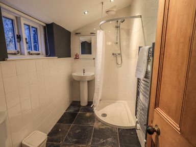 A bathroom with a shower, sink, towel radiator, small mirror, window, and a wooden door at Fairy Glen in Grasmere near Ambleside