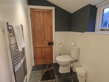 A bathroom with a toilet a wooden door a towel rack with a towel and a window at Fairy Glen in Grasmere near Ambleside