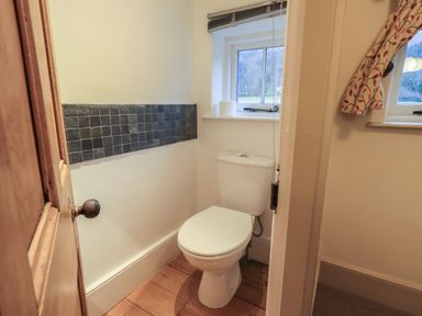 A small bathroom with a white toilet wooden floor and a window with a view at Fairy Glen in Grasmere near Ambleside