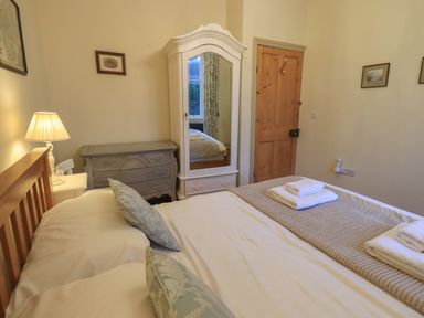 A bedroom with a wooden bed a white wardrobe with a mirror a grey dresser and a wooden door at Fairy Glen in Grasmere near Ambleside