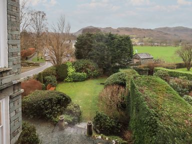 A garden with trimmed hedges wooden bench and trees near a road with hills in the background at Fairy Glen in Grasmere near Ambleside