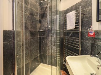 A bathroom with a glass shower enclosure black tiled walls a white sink with a faucet a towel on a heated rail and a bottle of hand soap at Fairy Glen in Grasmere near Ambleside